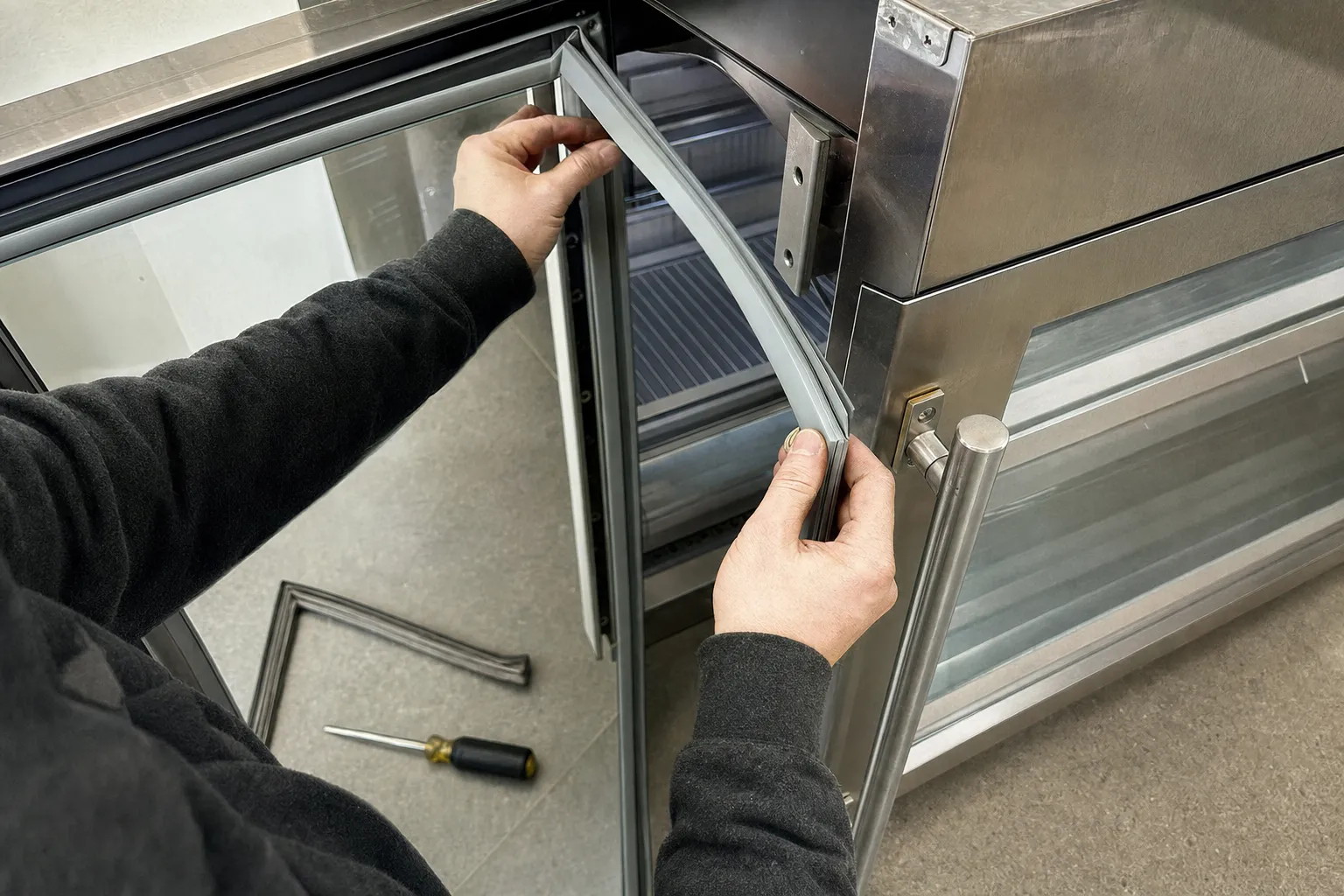 New grey door gasket being pressed into the frame of a stainless glass-door undercounter unit